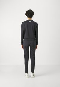 Námornícky teplákový komplet s dlhým rukávom a zúženými nohavicami, vyrobený z mäkkej tkaniny. Obsahuje logo na chrbte a rebrované manžety. Biele tenisky.