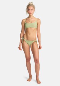 Svetlozelené rebrované bikiny s kratkým topom a nastavitelnými bokmi na viazanie. Materiál vyzerá hladko s minimálnym kovovým detailovaním.