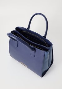 Ναυτικό μπλε δερμάτινη τσάντα χειρός με δύο επάνω λαβές, χρυσό φερμουάρ και πολλαπλές εσωτερικές θήκες. Δείχνει ανάγλυφο λογότυπο μπροστά.