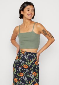 Top cropped verde-oliva com alças finas, combinado com uma saia floral caracterizada por flores laranja e folhagem verde sobre um fundo azul-marinho.