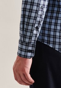 Blå och svart rutigt skjorttyg med en skräddarsydd passform, med knappmanschetter och en subtil logobrodering nära ärmen.