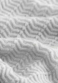 Graue Strickdecke mit einem strukturierten Zickzackmuster. Der Stoff ist weich und hat sichtbare Nähte, was ein gemütliches Aussehen verleiht.