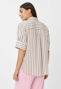 Chemise rayée en tissu marron et blanc, à manches courtes, avec des accents de boutons et un ourlet arrondi. Modèle de dos, montrant les détails du design à l'arrière.