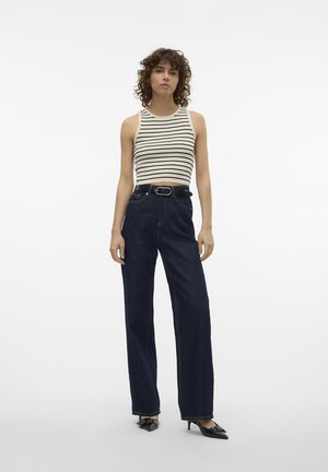 Randig ärmlös topp i kräm och svart, tillsammans med högmidjade mörkblå jeans. Innehåller ett svart bälte och spetsiga svarta klackar.
