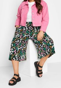 Rosa jeansjacka, vit skjorta, blommönstrade culottes i svart med flerfärgade blommor. Svarta sandaler med remmar fulländar outfiten.