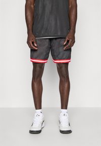 Sorte mesh atletikshorts med røde detaljer ved kanten, med en åndbar design. Båret med hvide sneakers og ankelsokker.