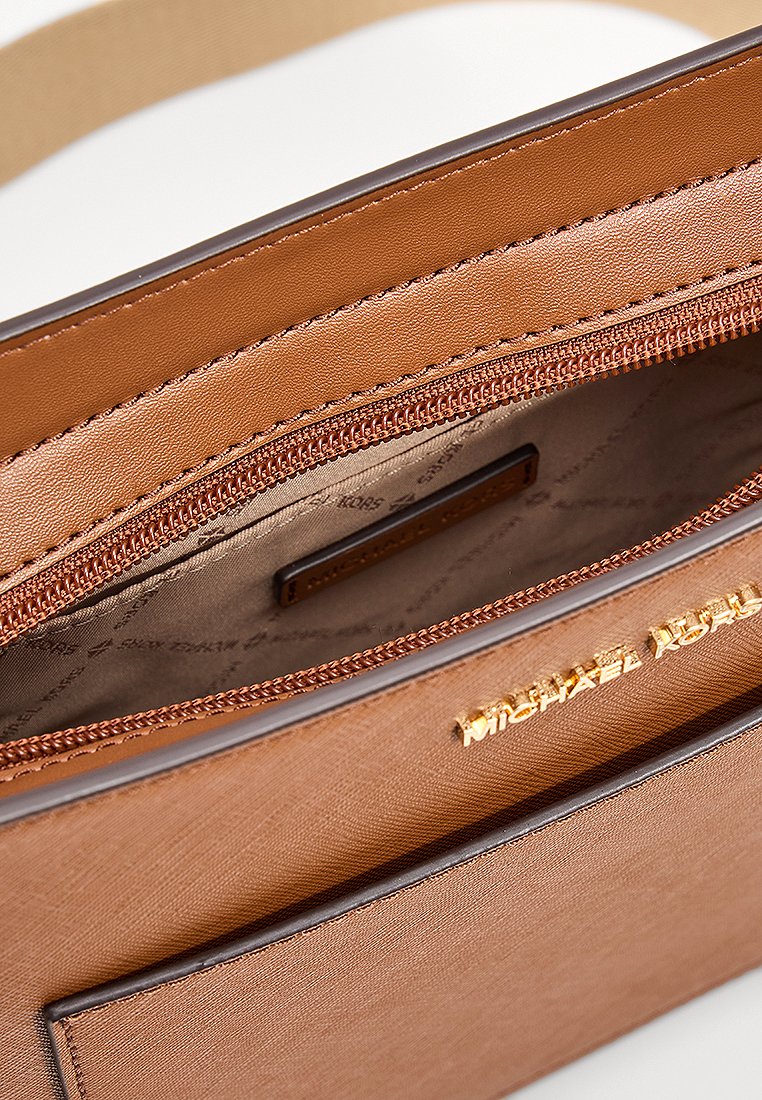 Sac en cuir marron Michael Kors avec logo doré, poche zippée visible et doublure intérieure en tissu beige avec impression de logo.