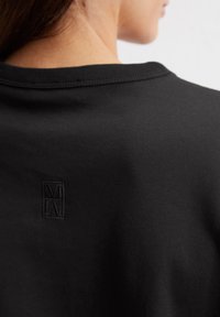 Zwarte t-shirt met een ronde halslijn, voorzien van een subtiel logo geborduurd in het zwart op de achterkant, gemaakt van zachte katoen.