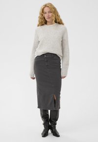 Sivý pletený sveter preložený cez tmavosivú džínsovú sukňu s rozparkom, doplnený čiernymi koženými čižmami po kolená. Jednoduchý dizajn s jasnými líniami.