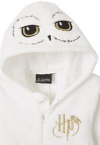 Weißer Fleece-Hoodie mit Eulengesicht-Design und gestickten Augen. Goldene Akzente umfassen das "HP"-Logo und Sternmuster auf dem Stoff.