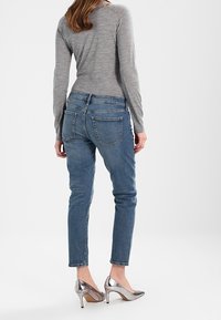 Maglietta grigia chiara a maniche lunghe abbinata a jeans aderenti blu, con un classico design a cinque tasche, e scarpe con tacco alto argento.