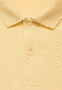 Žluté polo tričko, texturovaná tkanina, s žebrovaným límečkem a třemi knoflíky na výstřihu. Jednoduchý, klasický design s jemným povrchem.