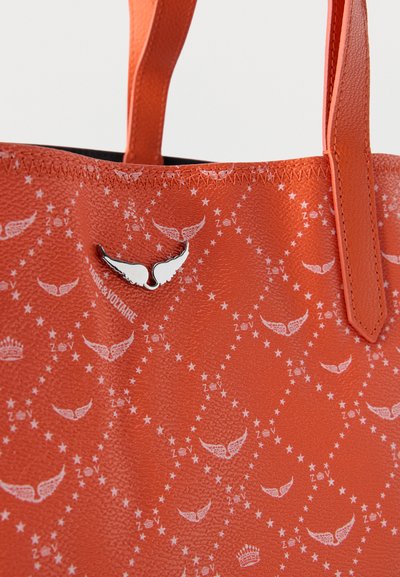 Sac à main en cuir orange avec motifs d'étoile et d'aile blancs, emblème métallique argenté en forme d'aile et poignées cousues.