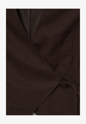 Donkerbruine wikkelstof met een geknoopt detail, die textuur en stiksel van een kledingstuk van dichtbij laat zien.