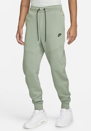 Helle grüne Nike Jogginghosen mit elastischem Bund, schwarzen Kordeln und Seitentaschen, kombiniert mit weißen Sneakers, die eine legere Passform zeigen.