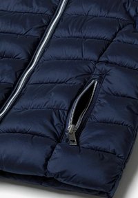 Marineblaue Pufferjacke mit gestepptem Design, ausgestattet mit einem zentralen silbernen Reißverschluss und einer seitlichen Reißverschlusstasche mit einem herzförmigen Zugband.
