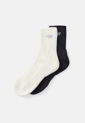 Ribbed socks in white and black. Each sock features a rounded toe and a small logo in a contrasting color near the top.