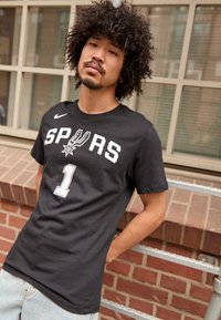 Sort kortærmet T-shirt med "SPURS" og nummer "1" i hvidt tryk, med et Nike-logo på venstre skulder. Uformeligt bomuldsstof.