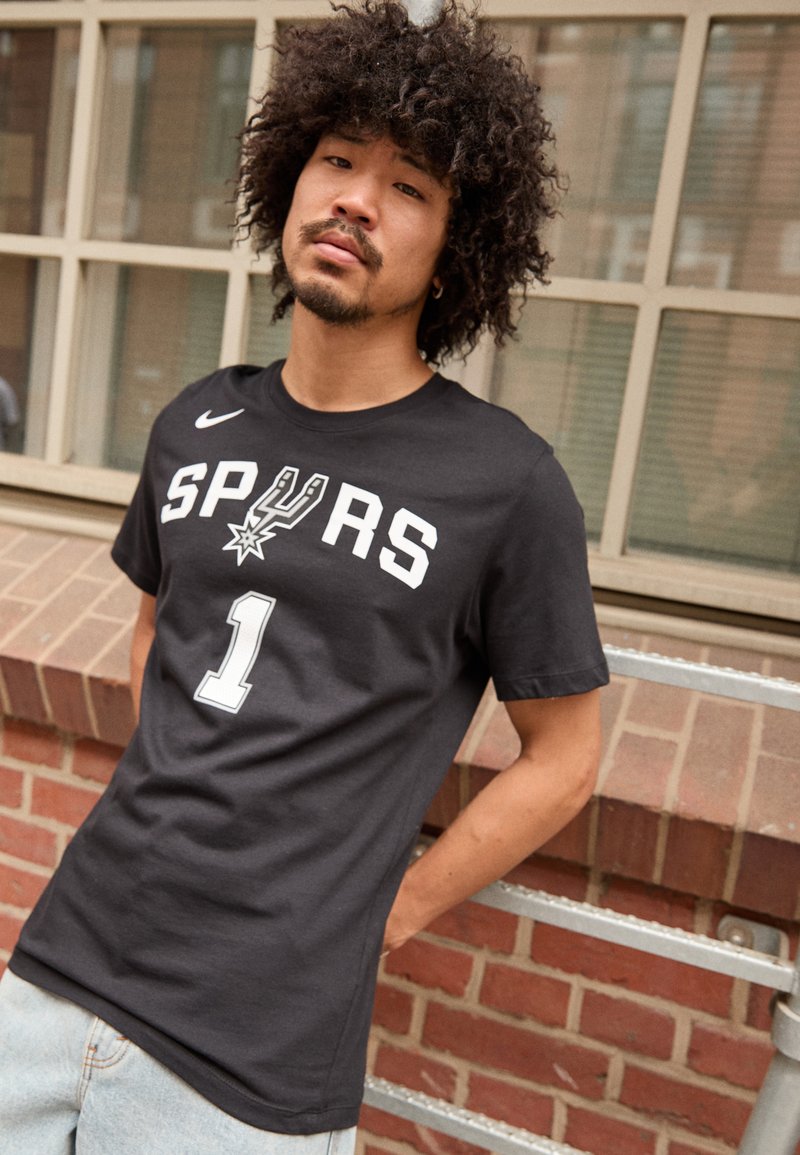 Sort kortærmet T-shirt med "SPURS" og nummer "1" i hvidt tryk, med et Nike-logo på venstre skulder. Uformeligt bomuldsstof.