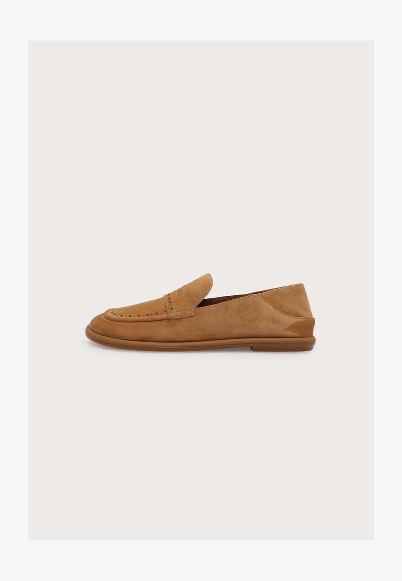 Mocassin en daim beige clair avec une semelle en caoutchouc basse, des coutures apparentes et un détail fente à penny classique, présenté en profil gauche sur fond blanc.