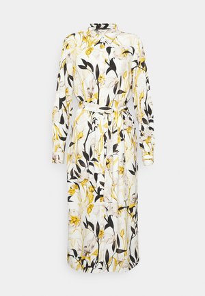 Robe blanche à manches longues avec un motif floral en jaune, noir et gris. Elle possède un col et une ceinture assortie à la taille.