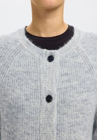 Light gray knitted cardigan with a soft texture, featuring a round neckline and three black buttons down the front.