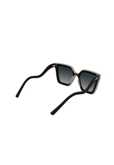 Lunettes de soleil oversize noires et beiges avec une monture géométrique, des verres dégradés et des branches noires flexibles. Accent doré sur le côté.