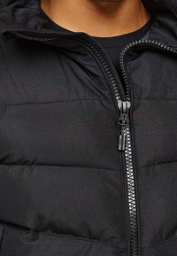 Černá prošívaná bunda s texturovaným povrchem, plným zapínáním na zip a kapucí. Materiál vypadá odolně a voděodolně.