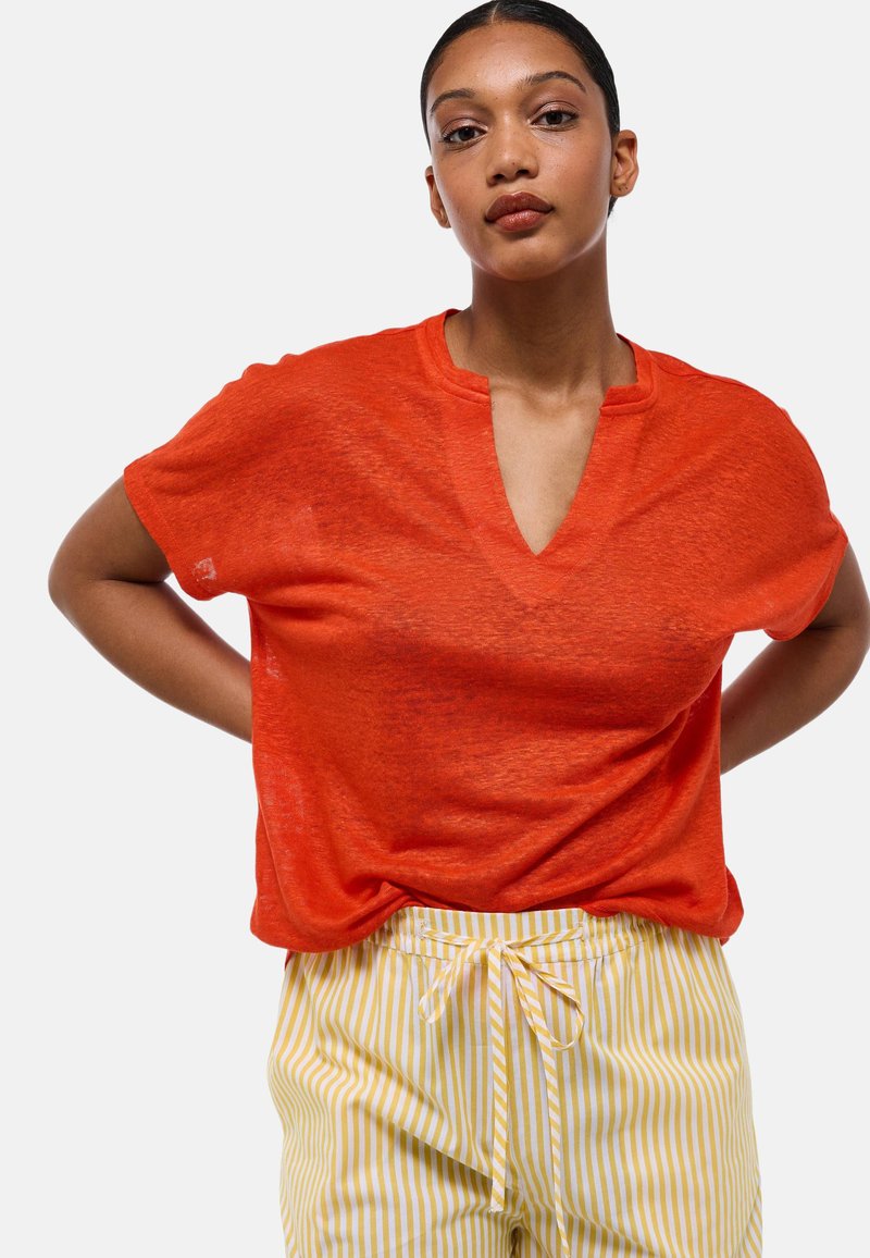 Haut rouge à manches courtes avec un décolleté en V. Tissu léger et légèrement transparent. Assorti à un pantalon à cordon de serrage rayé jaune et blanc.