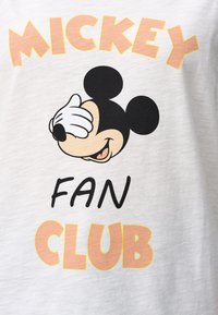Witte T-shirt met een cartoon van Mickey Mouse die met zijn hand zijn ogen bedekt. Tekst "MICKEY FAN CLUB" in gele en zwarte blokletters.