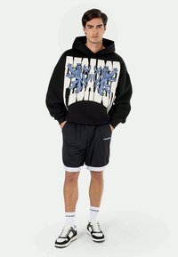 Black hoodie with blue lion graphic and white text, paired with black shorts featuring white trim, and black sneakers with white accents.