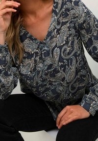 Camicia a maniche lunghe con scollo a V in blu navy scuro, caratterizzata da intricati motivi paisley in blu chiaro e beige, realizzata in un morbido tessuto testurizzato.