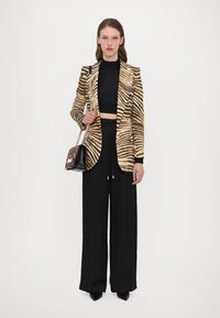 Blazer met een tijgerprintpatroon in beige en bruin, gecombineerd met zwarte wijde broek en een zwarte handtas met kettingriem.
