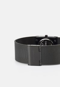 Orologio con cinturino in rete nera, cassa quadrata, quadrante scuro e dettagli argentati. Presenta una chiusura con incisione "Calvin Klein".