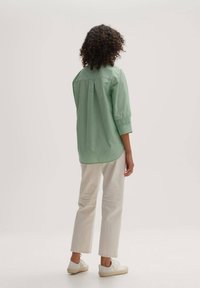 Ljusgrön skjorta med knappar och trekvartslång ärm, med en bakfåll, och parat med vita raka byxor och vita sneakers.