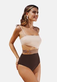 Hoch taillierter Badeanzug in Beige und Braun, mit einem Cutout-Design und metallischen Hardware-Akzenten an der Taille. Glatte Stofftextur.