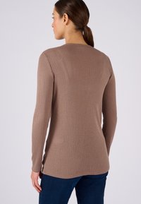 Maglione a maniche lunghe a coste in marrone, con scollo rotondo e orlo leggermente curvo, abbinato a jeans blu scuro.