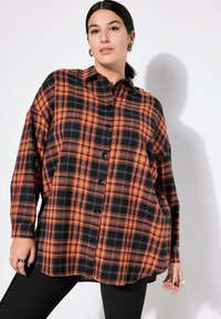 Camicia a quadri in flanella nera e arancione, con chiusura frontale a bottoni, colletto e vestibilità ampia. Maniche lunghe con polsini a bottoni.