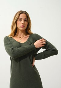 Maglione a coste verde oliva con maniche lunghe e scollo a V. Presenta una texture sottile e una vestibilità rilassata.