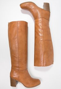 Bottes en cuir marron montantes avec un bout arrondi, un talon carré et des coutures latérales. Elles présentent une texture lisse et des surpiqûres contrastées.