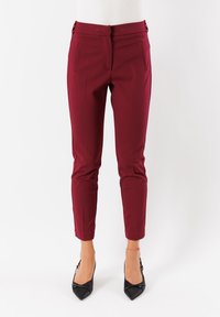 Pantaloni slim-fit bordeaux a lunghezza caviglia con tasche laterali, abbinati a décolleté nere a punta su uno sfondo bianco.