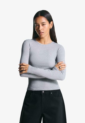 Long-sleeve, fitted gray top in soft fabric, featuring a round neckline and seamless design. Paired with black pants and silver rings.