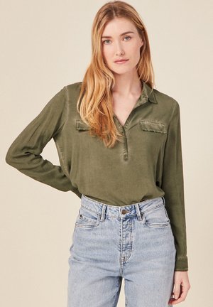 Olivgrünes Langarmhemd mit Kragen, ausgestattet mit zwei Brusttaschen und einem lockeren Schnitt, kombiniert mit hochgeschnittenen hellen Jeans.