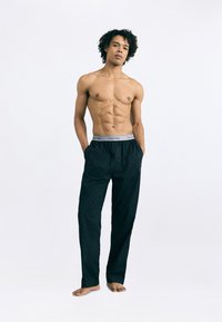 Čierne vzorované pyžamové nohavice s elastickým pásom a šedým logom "Calvin Klein". Model stojí naboso s rukami v vreckách.