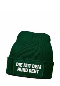 Green knit beanie with a folded cuff, featuring a prominent white text patch that reads “DIE MIT DEM HUND GEHT.” Vertical ribbed texture throughout.