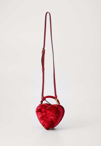 Sac crossbody en forme de cœur en velours rouge, avec une texture lisse, une courte poignée et une longue sangle réglable. Détails en métal doré.