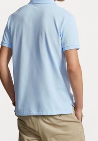 Vaaleansininen polo-paita, jossa on teksturoitu kangas, lyhyet hihat ja kaulus. Paitassa on sivuaukot ja hienovarainen kiilto.