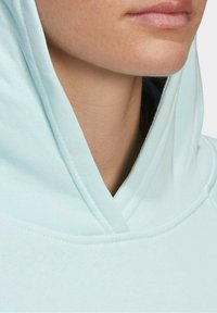 Sweat à capuche bleu clair avec une grande capuche, présentant une texture lisse et un détail cousu autour de l'encolure, zone du col partiellement visible.