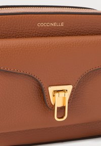 Brown leather handbag with textured finish, gold hardware, and a distinctive clasp. Features a subtle brand logo embossed on the front.