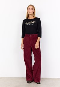 Black long-sleeve shirt with "ELEMENTS OF STYLE" text, paired with wide-leg burgundy corduroy pants, featuring a button detail and textured fabric.